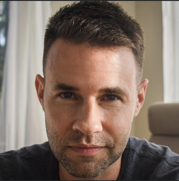 headshot photo of Sean Mackey. Sunny day, short brown hair, brown eyes, light stubble, gray shirt